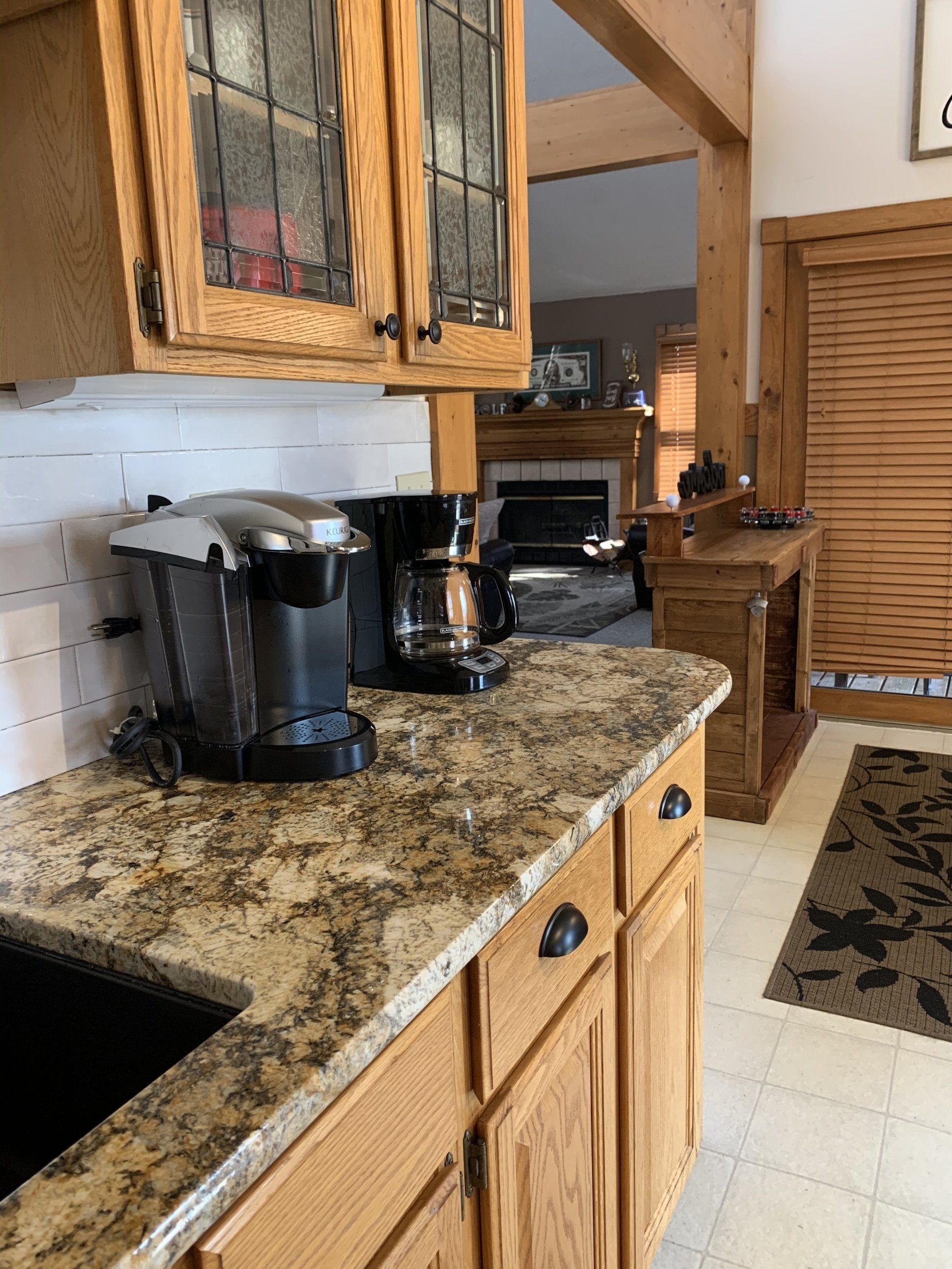 Kitchen with granite countertop, wooden cabinets, Keurig, coffee maker, and fireplace in the background.
