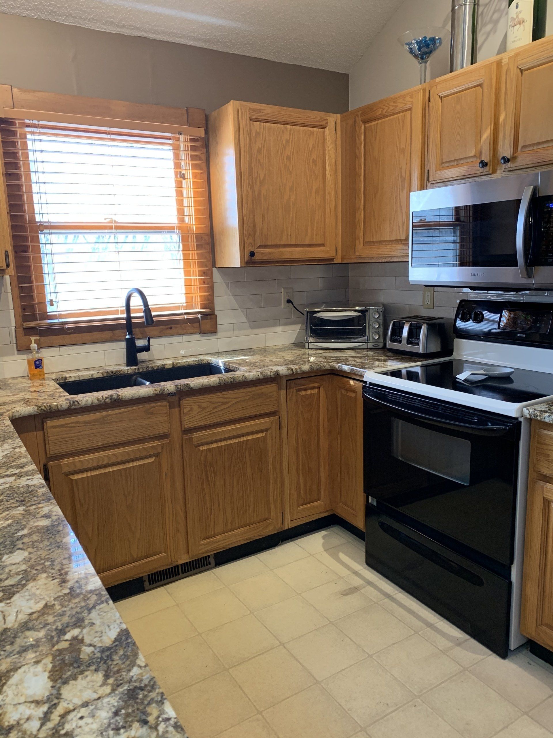 Kitchen with wooden cabinets, black appliances, and a window with blinds.