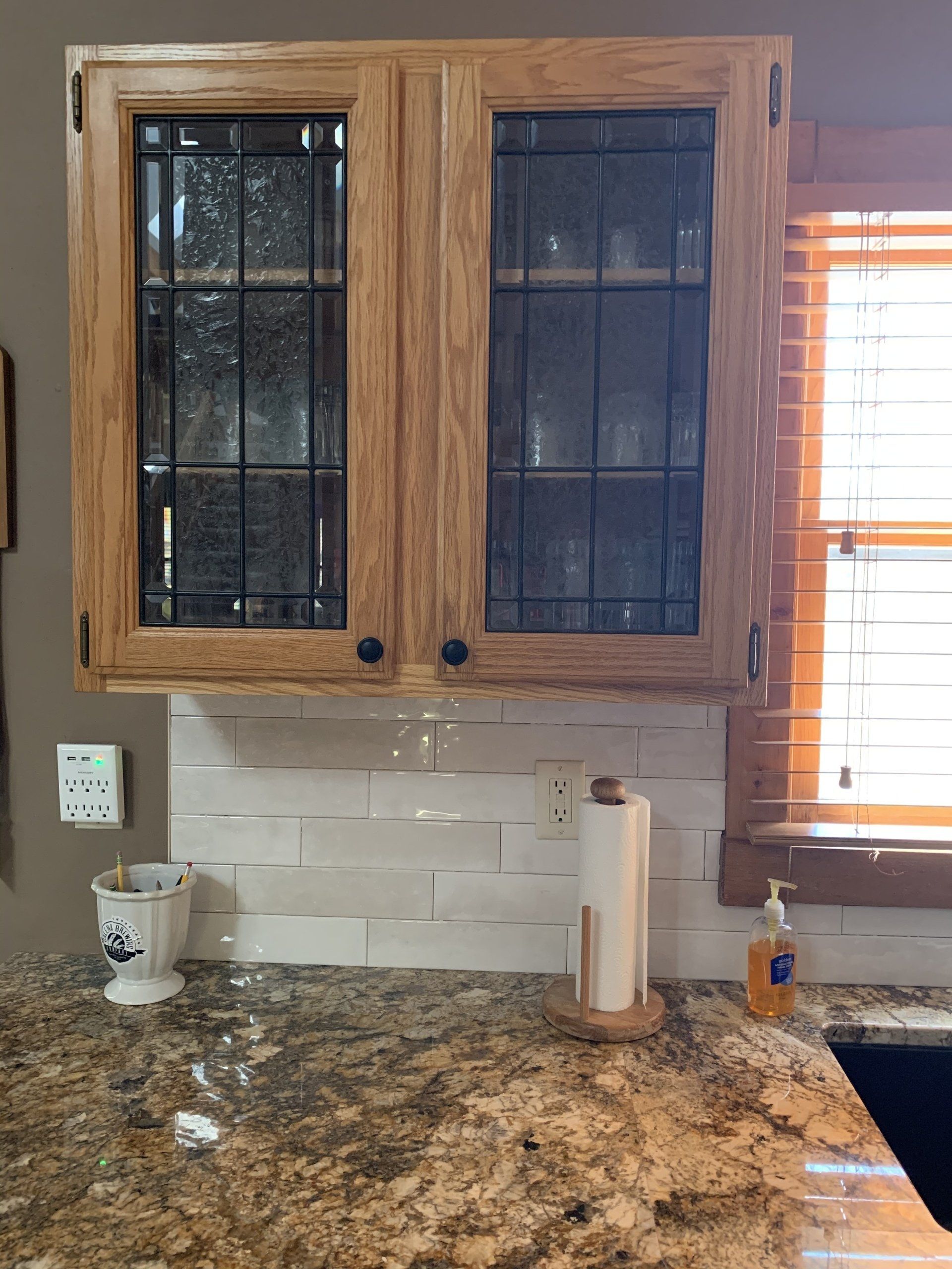 Kitchen cabinets with glass doors, above a countertop, and backsplash tiles.