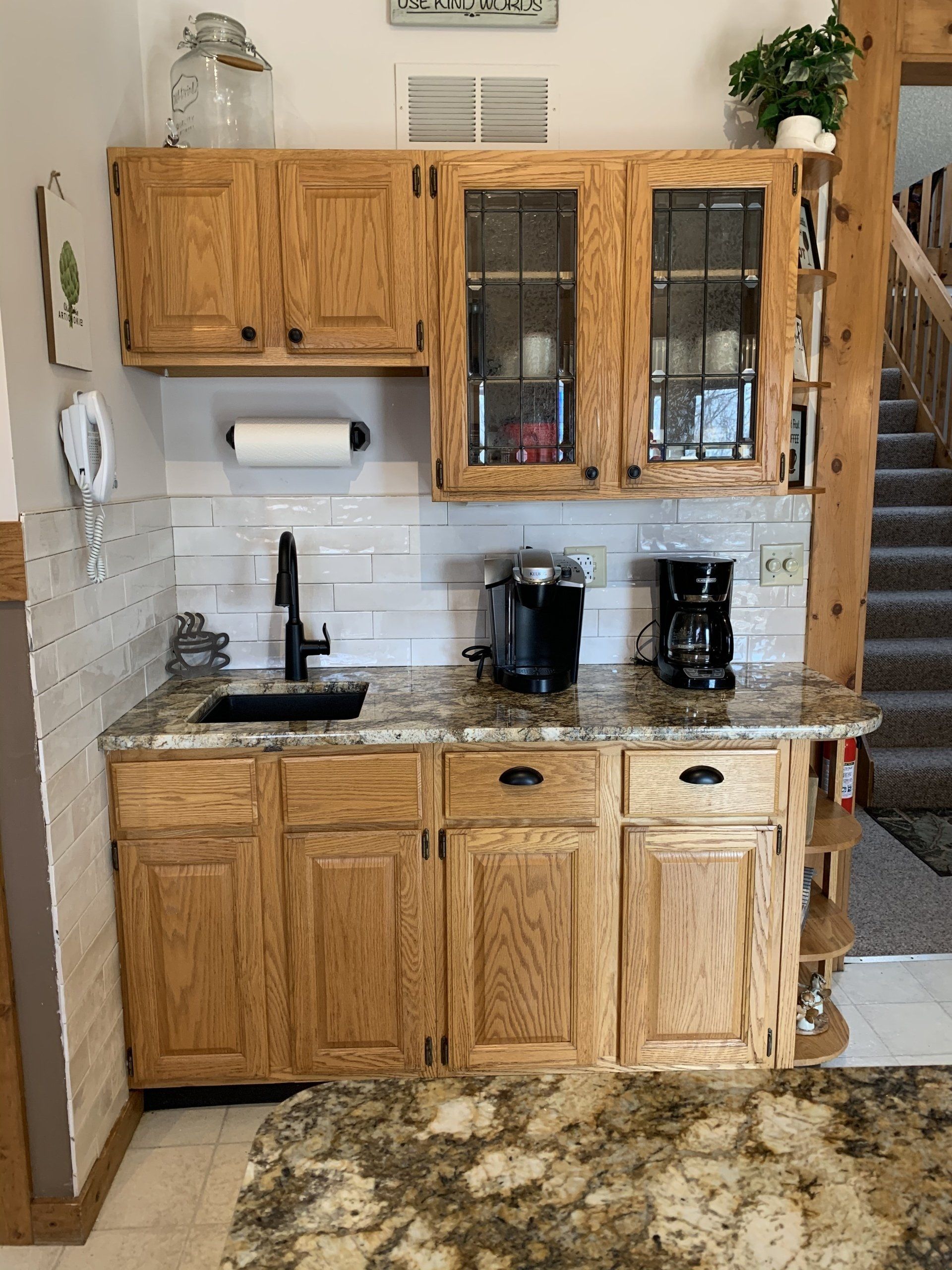 Small kitchen area with wood cabinets, granite countertop, sink, and coffee makers.