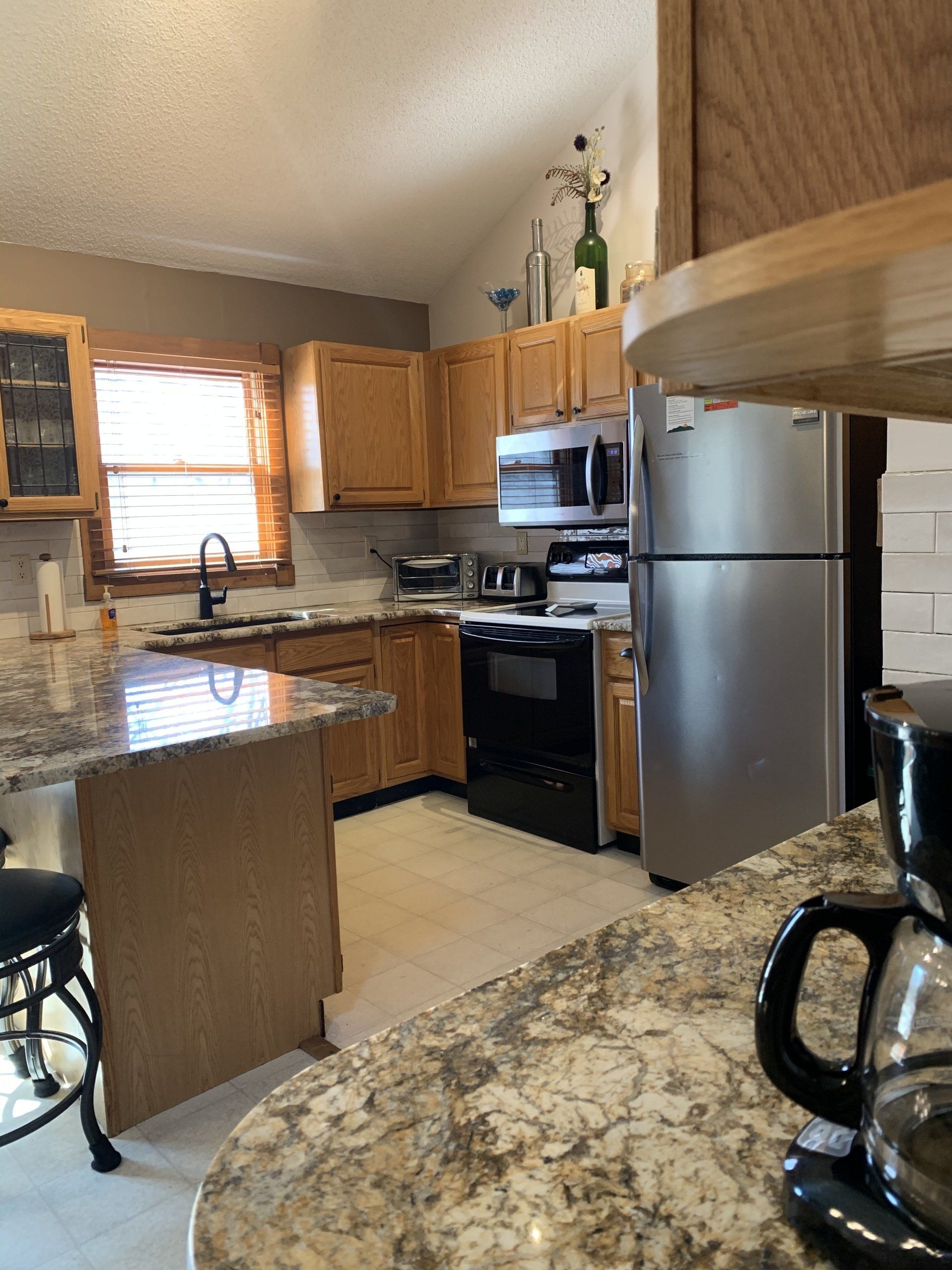 Kitchen with light wood cabinets, stainless steel refrigerator, and granite countertops.