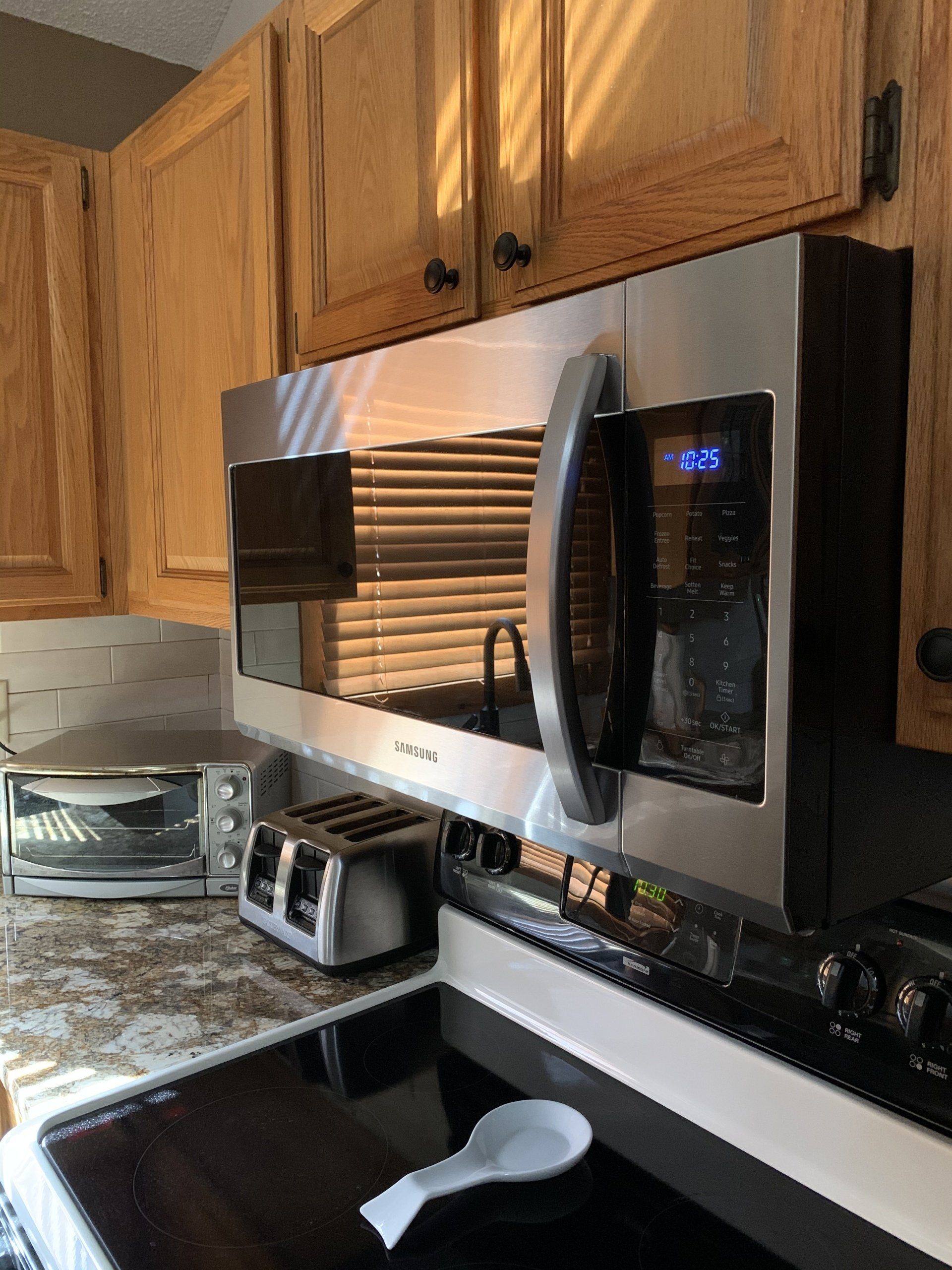Stainless steel microwave above stovetop in kitchen, with toaster and countertop.