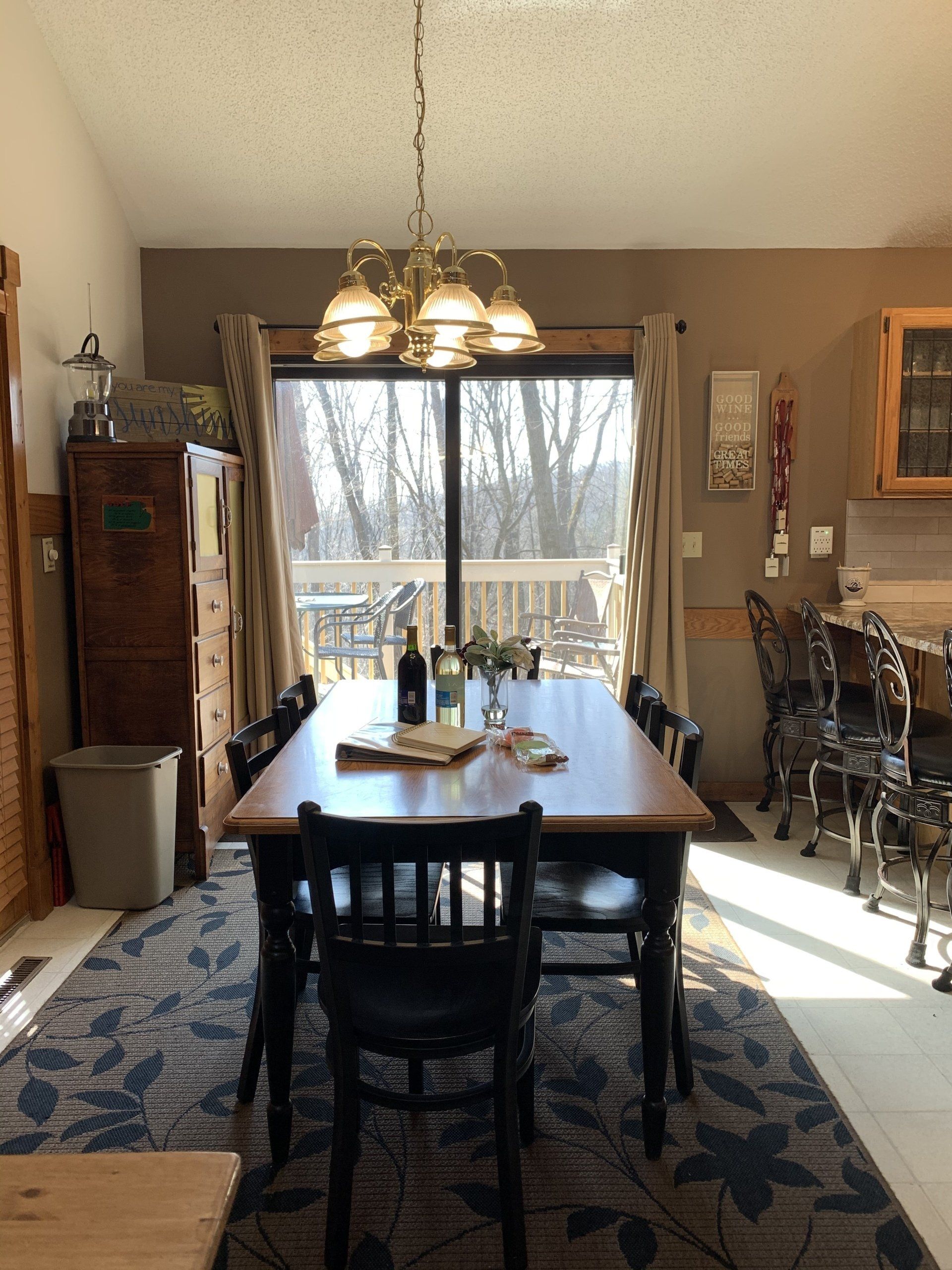 Dining room with table and chairs, window overlooking trees, chandelier, rug, and cabinet.