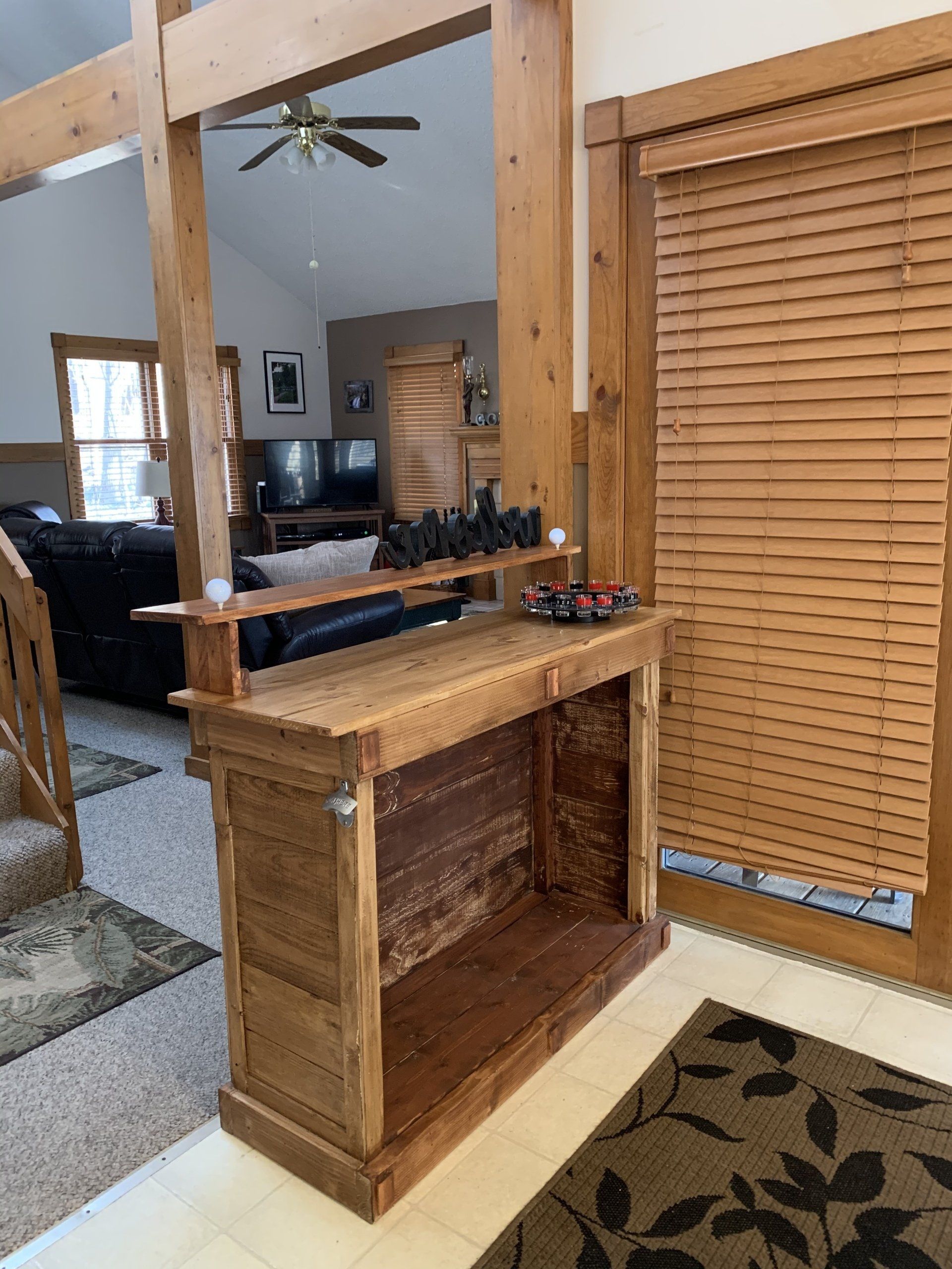 Wooden bar with shelf, against a wall. Shelves hold decor. Door with blinds on right, opening to living room.