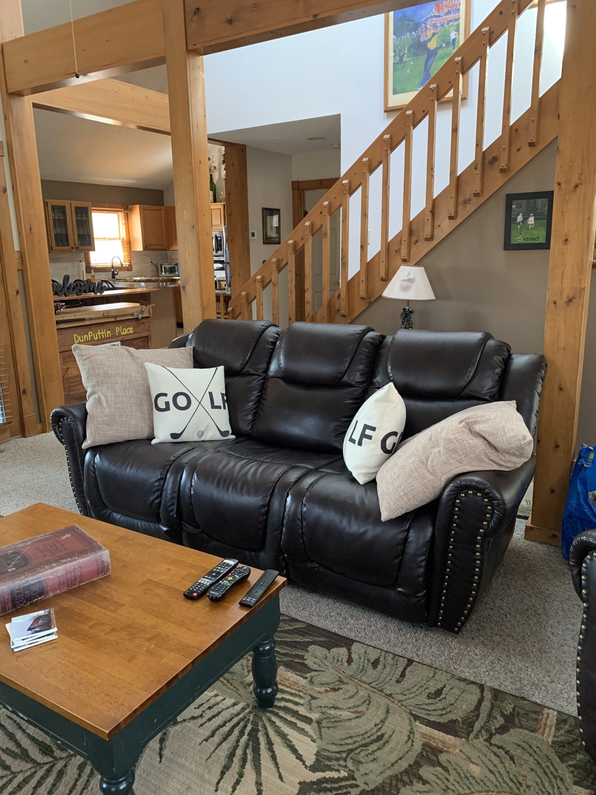 Living room with a dark leather sofa, pillows, and wooden coffee table. Staircase leads up.