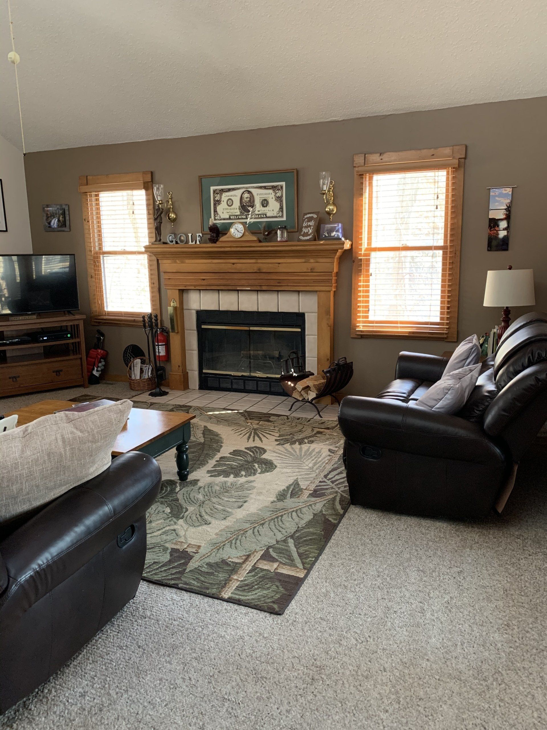 Living room with fireplace, brown wall, two windows, two brown leather recliners, and patterned rug.