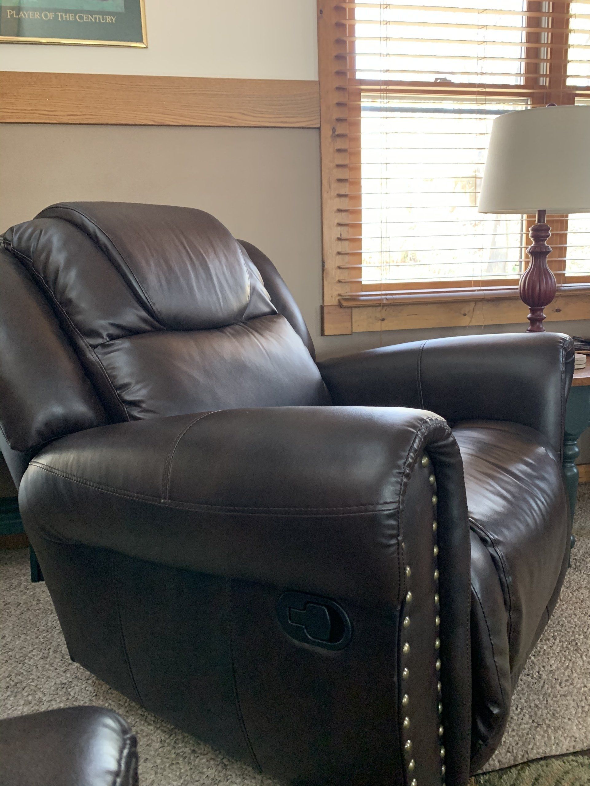 Dark brown leather recliner chair in a room with a window and a lamp.