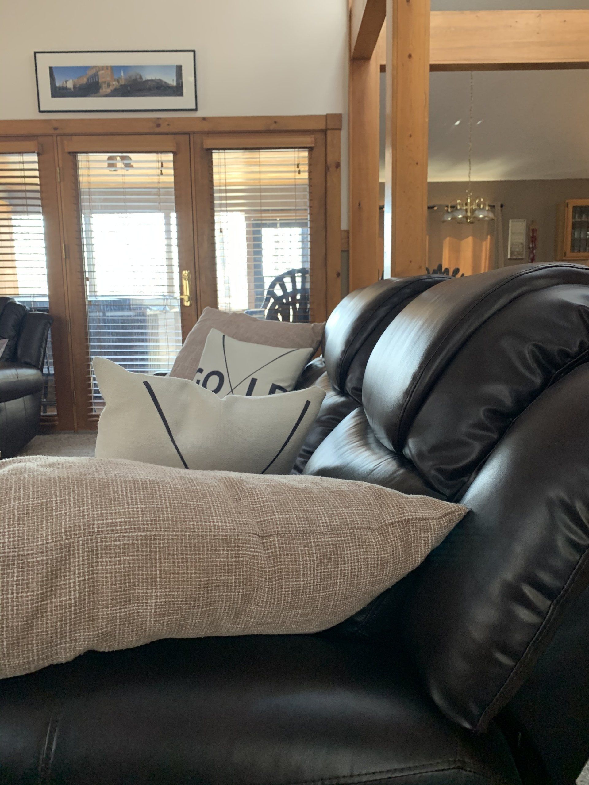 Cozy living room with brown leather sofa, pillows, throw, and view to a doorway.