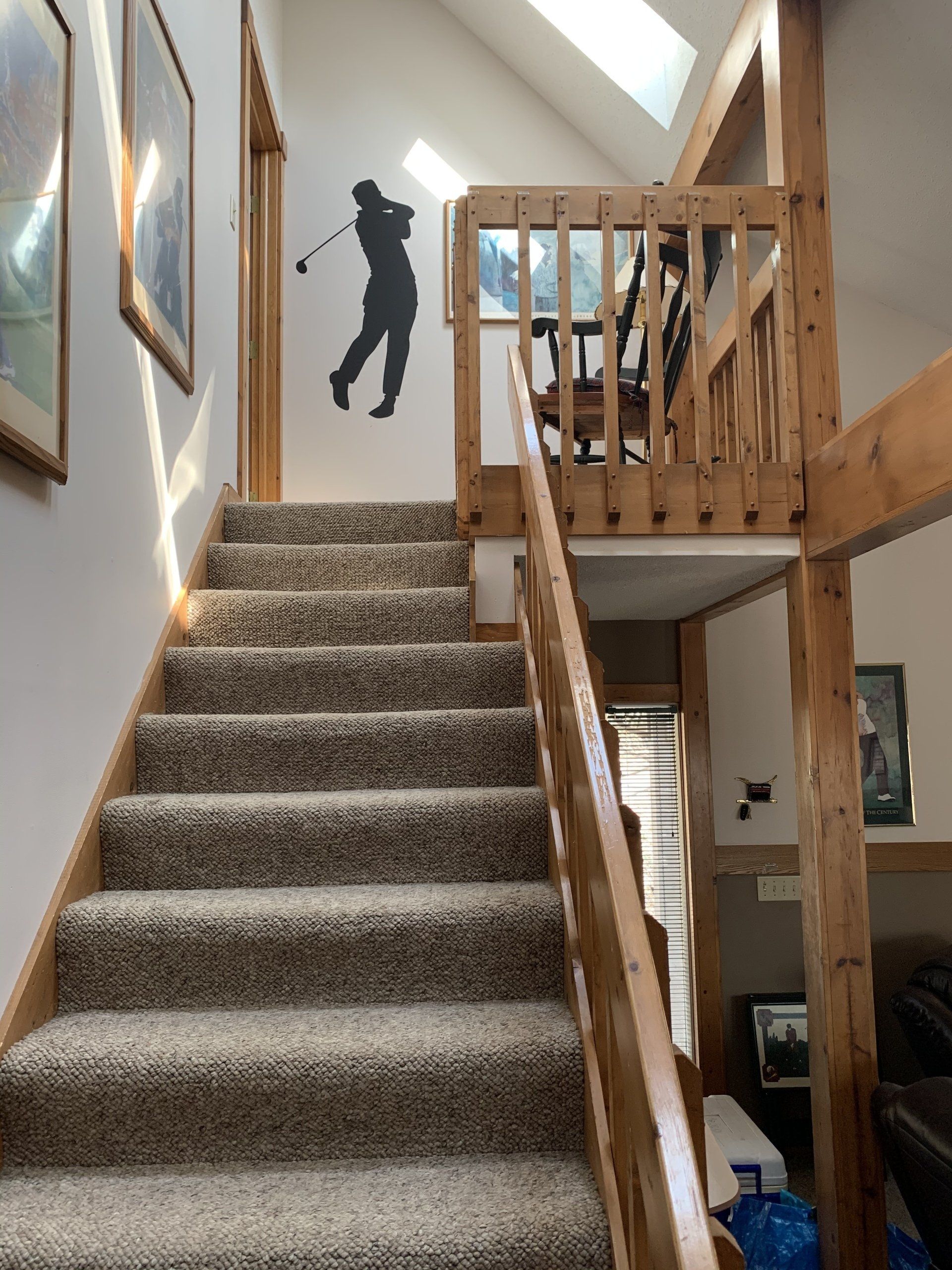 Staircase with carpet leads to a loft. A golf swing silhouette is on the wall. Wooden railings and trim.