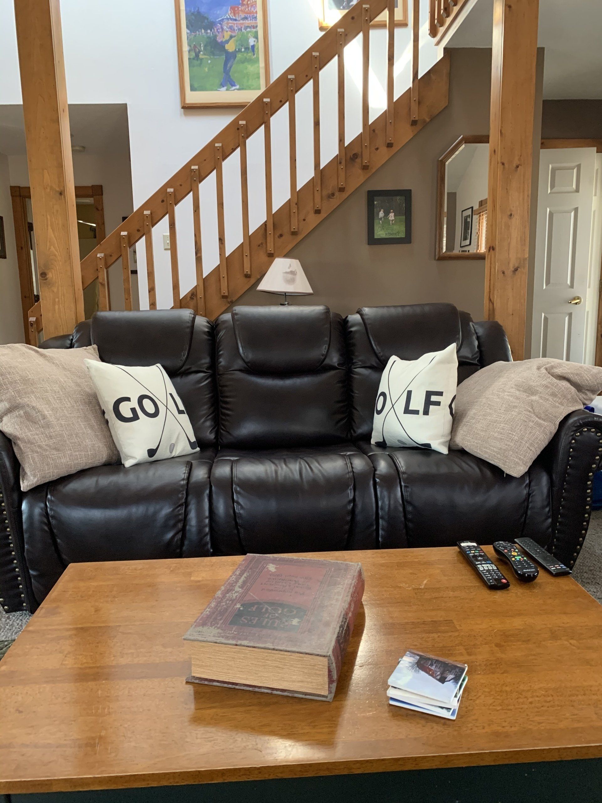 Living room with leather sofa, coffee table, and staircase in background.