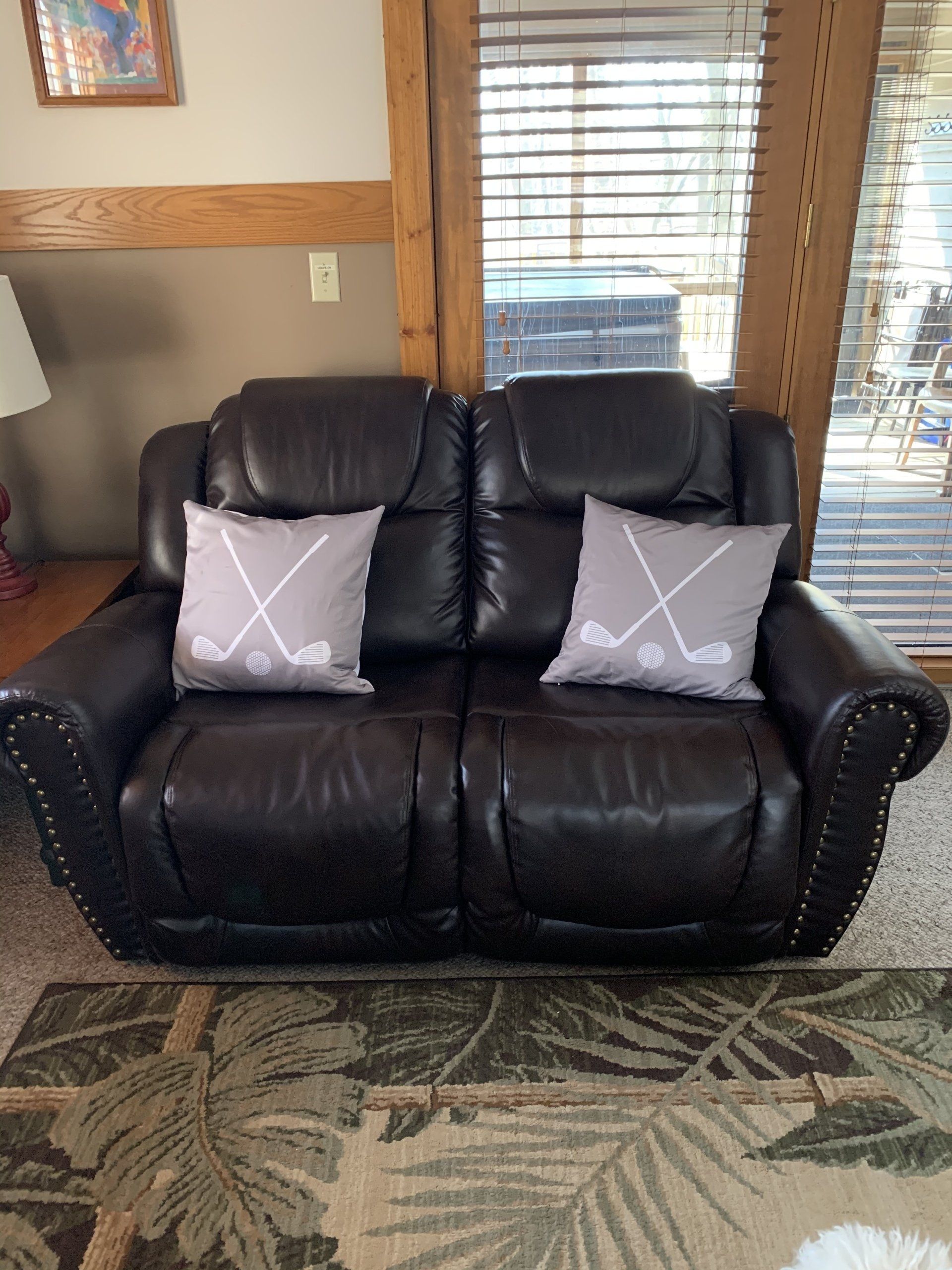 Dark brown leather loveseat with two gray hockey stick pillows, on patterned rug.