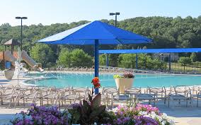 Blue umbrella over a pool, with chairs, waterslide, and trees in background.