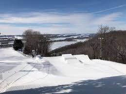 Snowy ski slope with small jumps, overlooking a winter landscape of fields and trees.