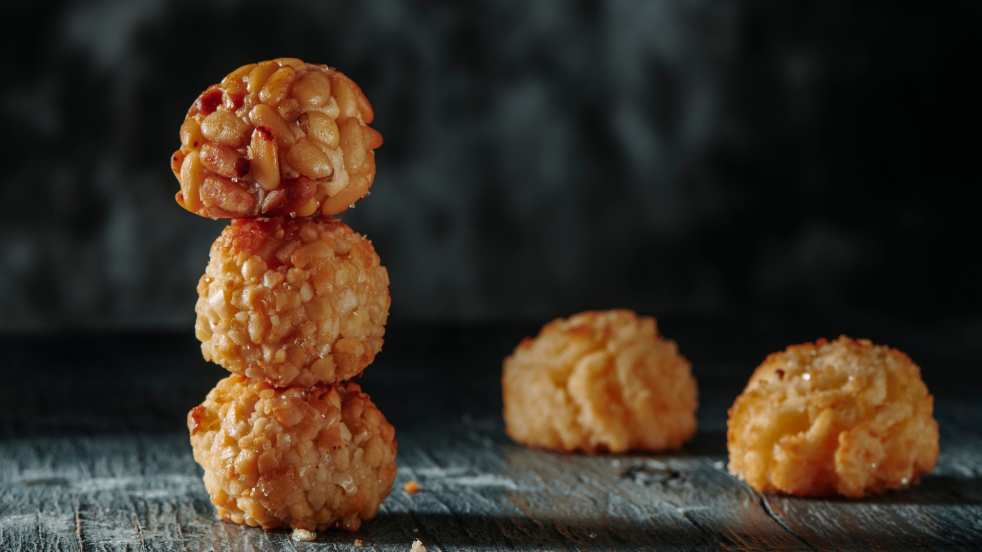 Tres galletas doradas con sabor a nuez apiladas, con dos galletas más al lado de ellas sobre una superficie de madera.