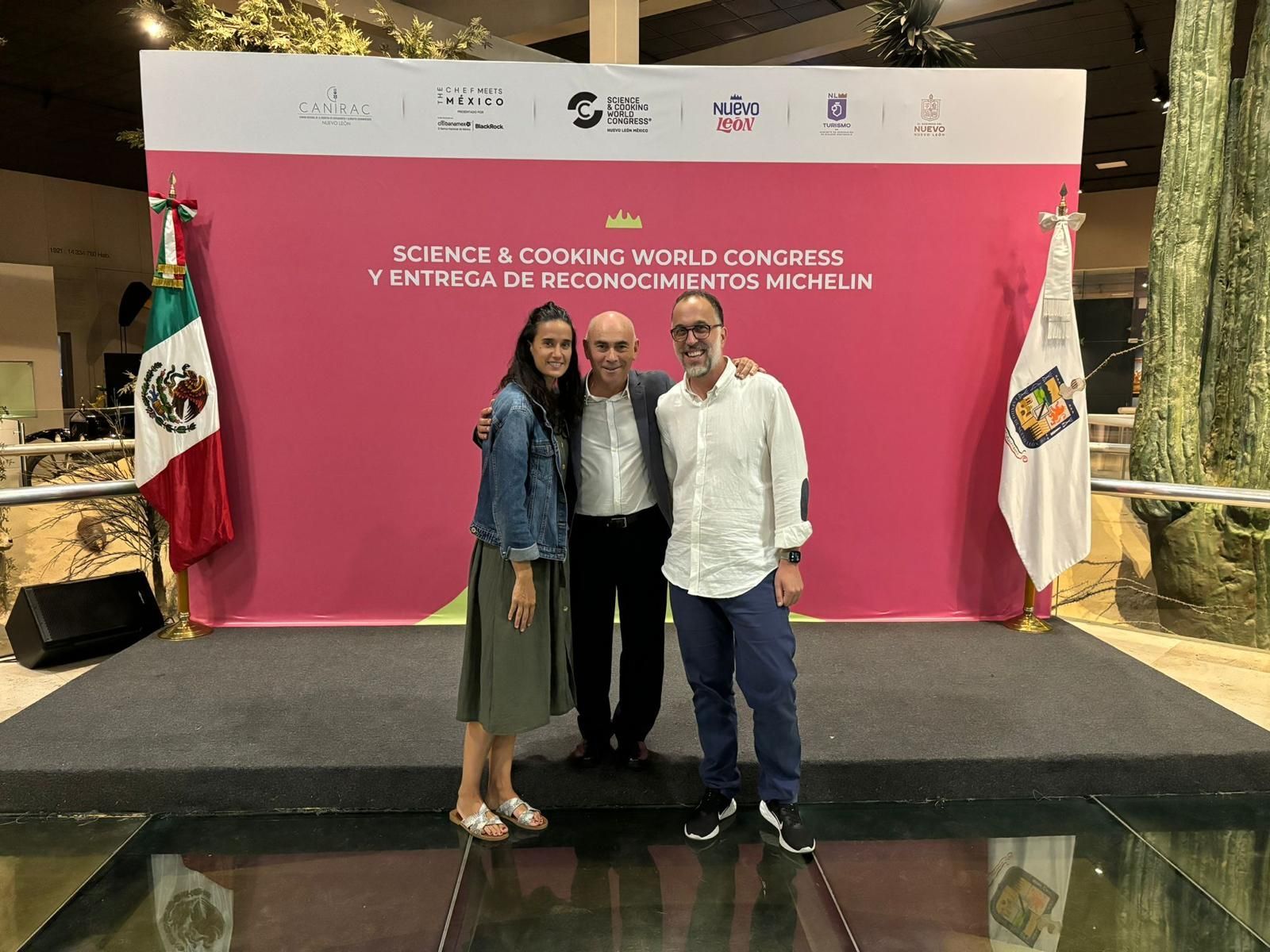 Tres personas posan para una foto frente a una pared rosa.