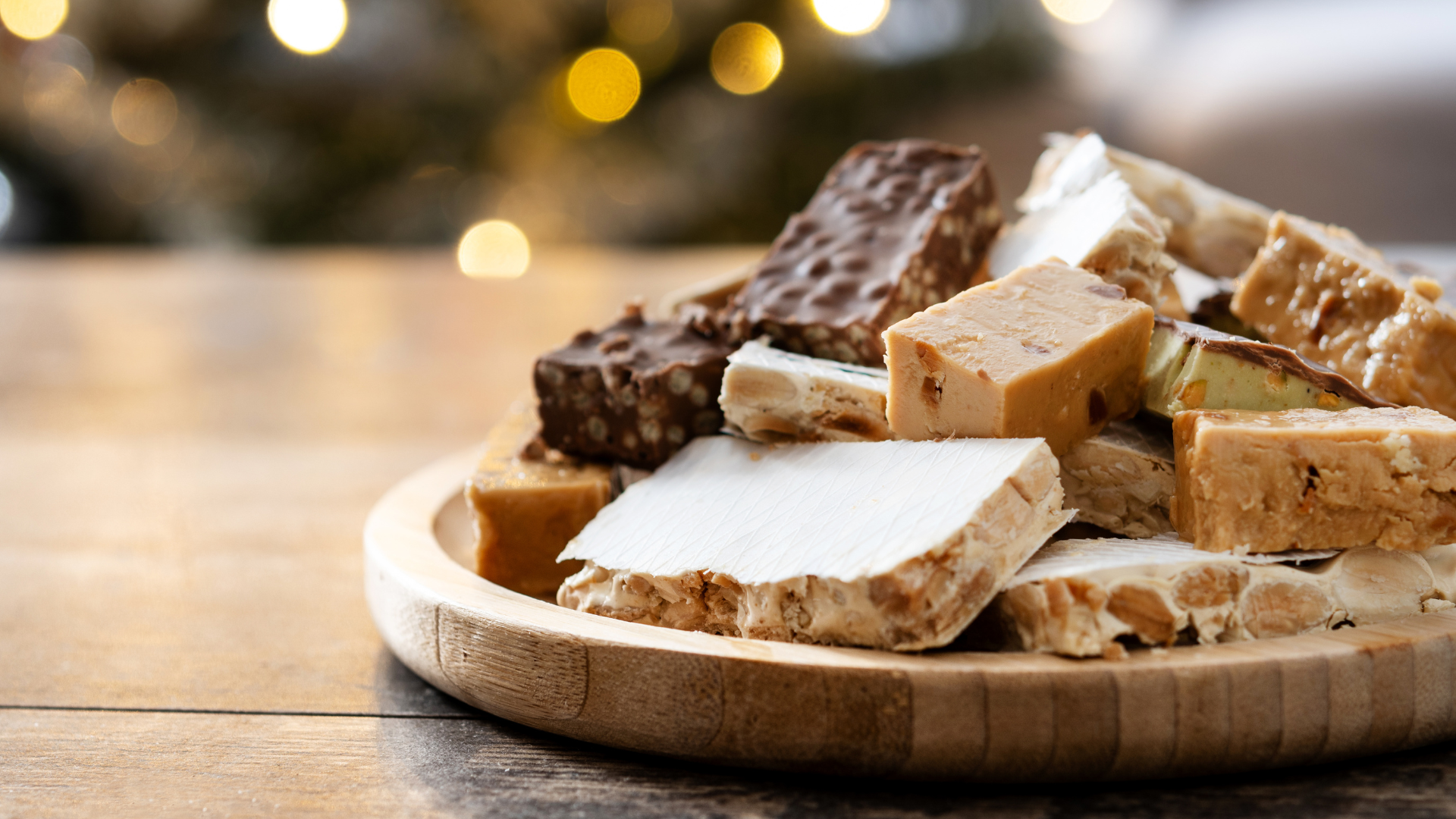 Assorted nougat on a wooden plate, with bokeh lights in the background.