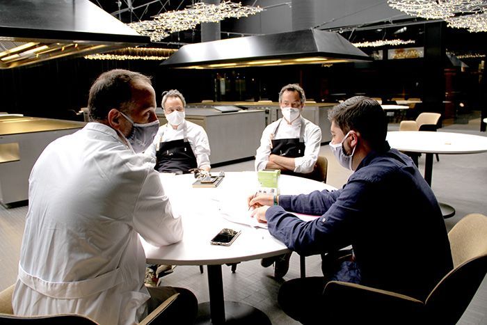 Un grupo de personas que llevan mascarillas están sentadas alrededor de una mesa.