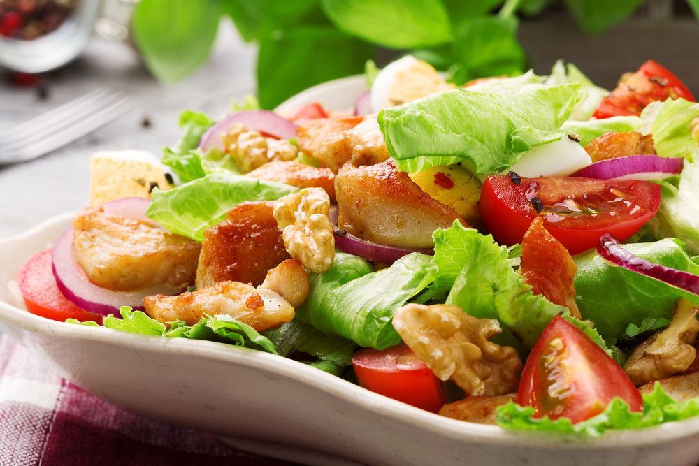 Una ensalada con pollo, lechuga, tomates, cebollas y nueces en un plato.