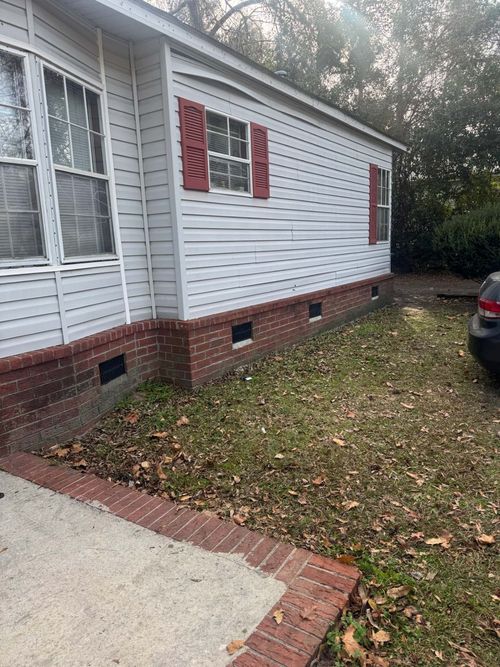 Exterior view of a white-sided house with red shutters, a brick foundation, and a concrete patio walkway.