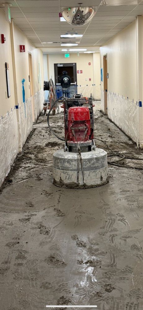 Damaged hallway under repair, with debris, exposed floor, and a red construction machine in the center.