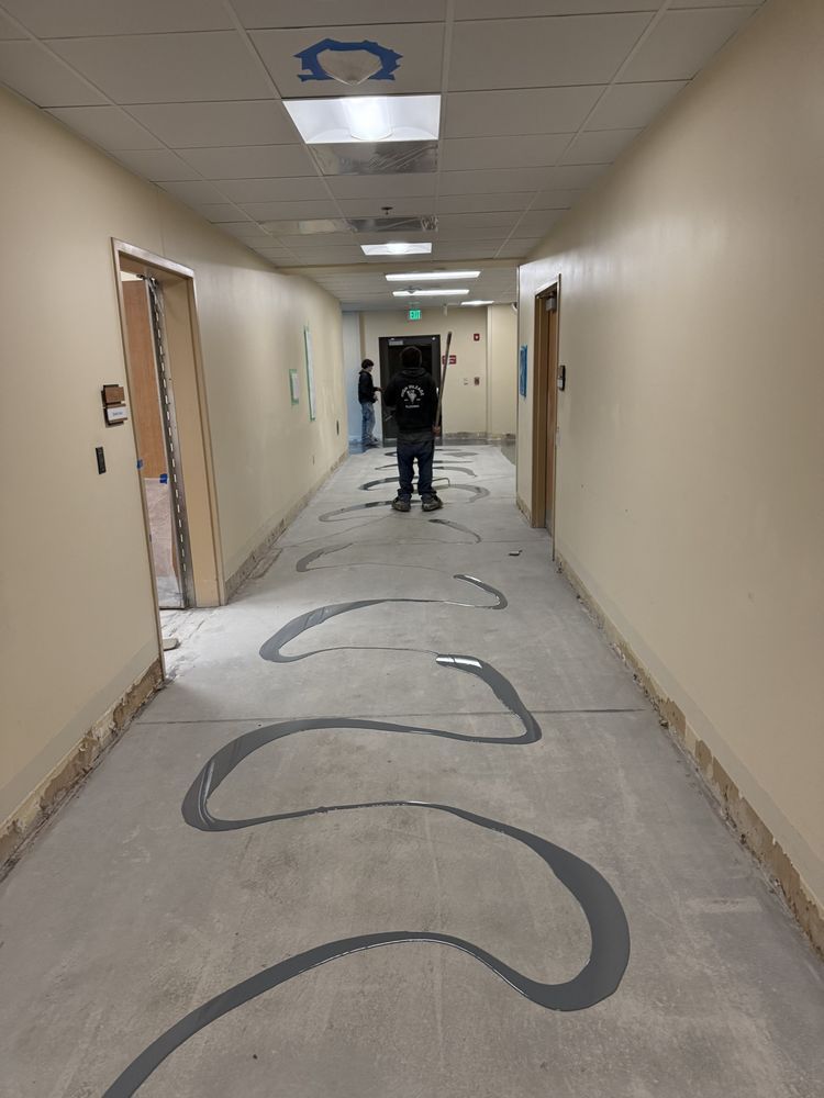 Hallway with large black squiggle painted on floor, fluorescent lights, and a person walking away in the distance