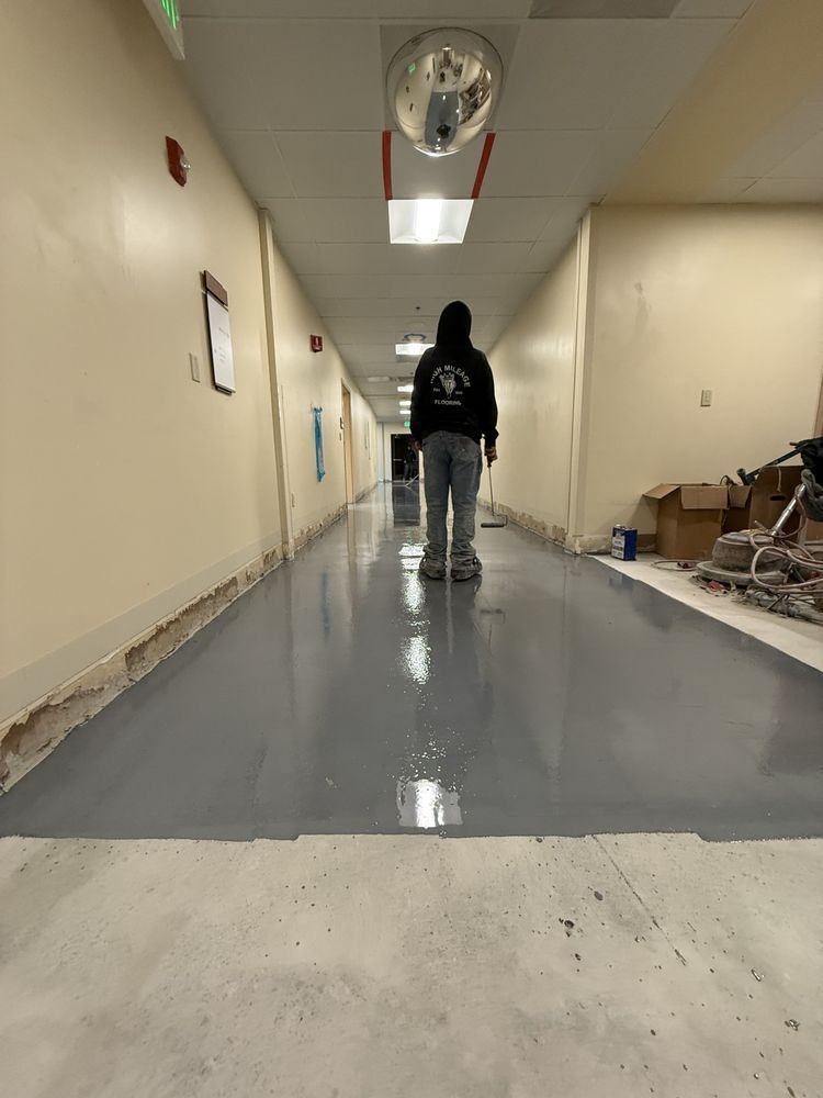 Person walking down a long hallway with a glossy gray floor and ceiling lights, carrying a backpack