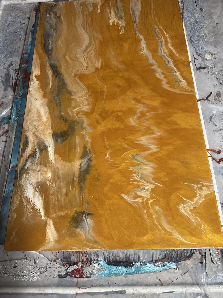 Abstract marbled resin panel in gold, white, and dark green tones on a work surface
