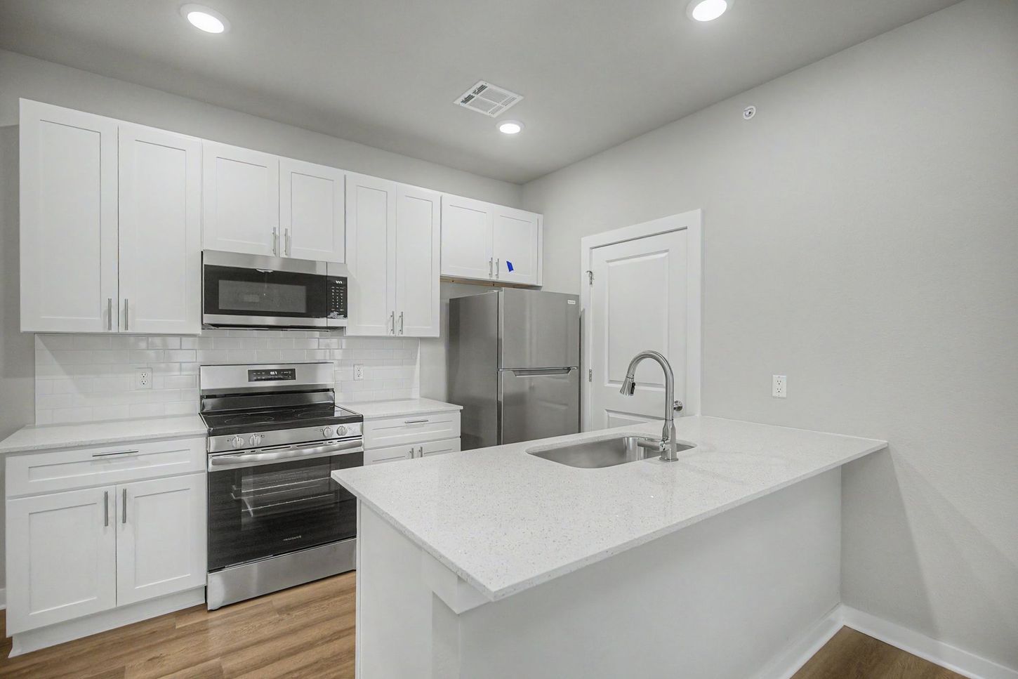 Bright white modern kitchen with stainless steel appliances, island, and wood floor