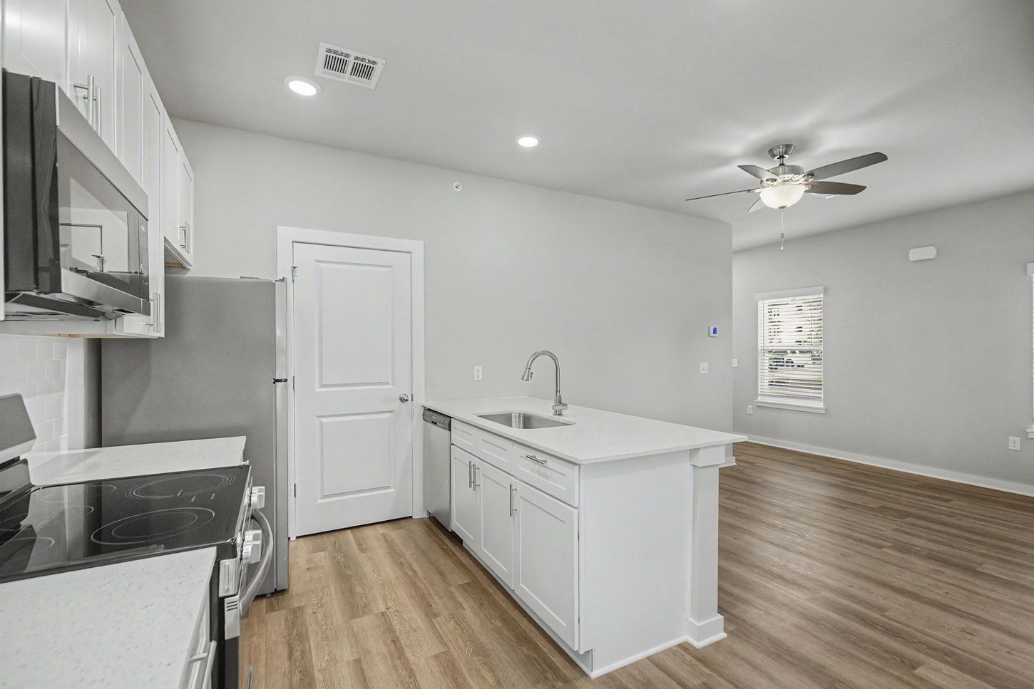 Bright modern kitchen with white cabinets, island sink, stainless appliances, and open living area.