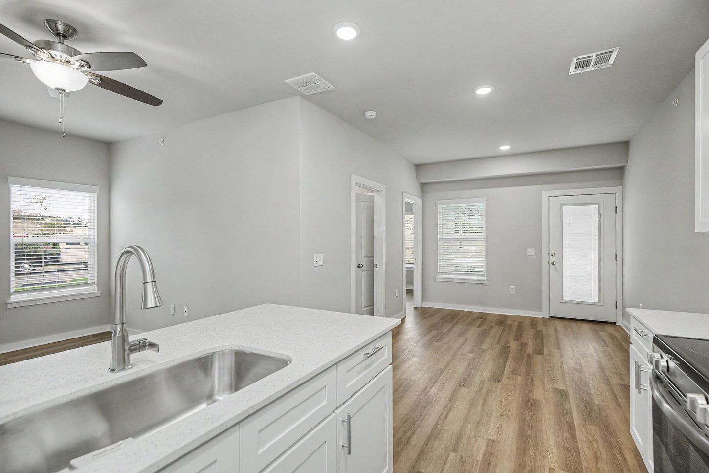 Bright open kitchen and living area with white cabinets, stainless sink, and wood floors