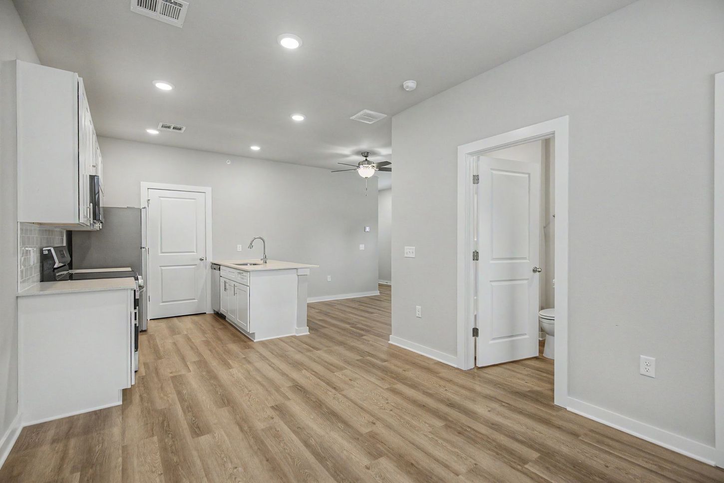 Bright modern kitchen with white cabinets, island, and wood-look flooring in an open room