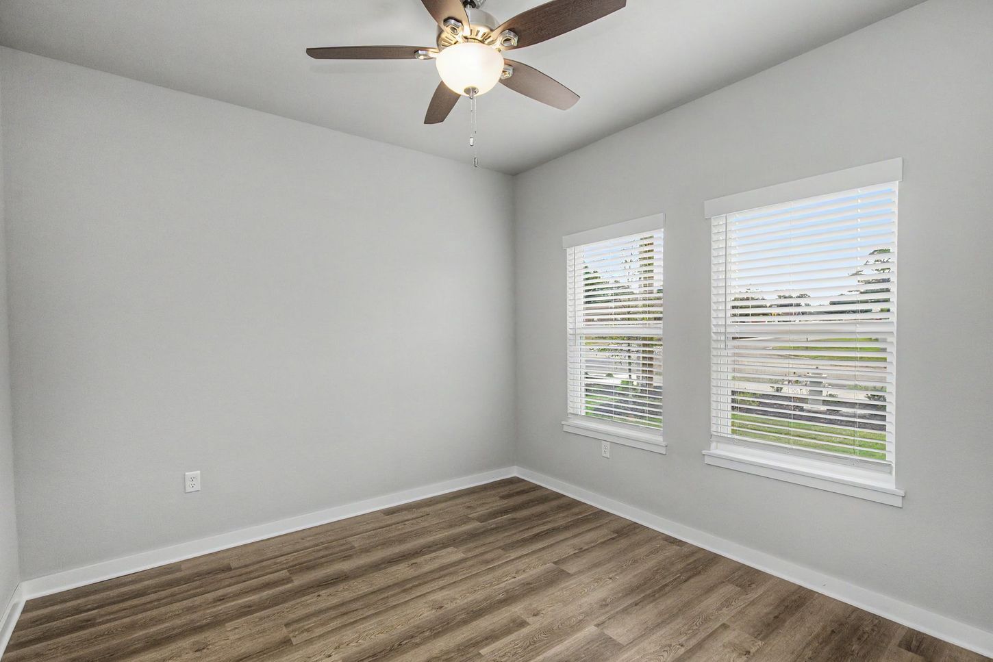 Empty bedroom with gray walls, wood-look flooring, ceiling fan, and two windows with white blinds