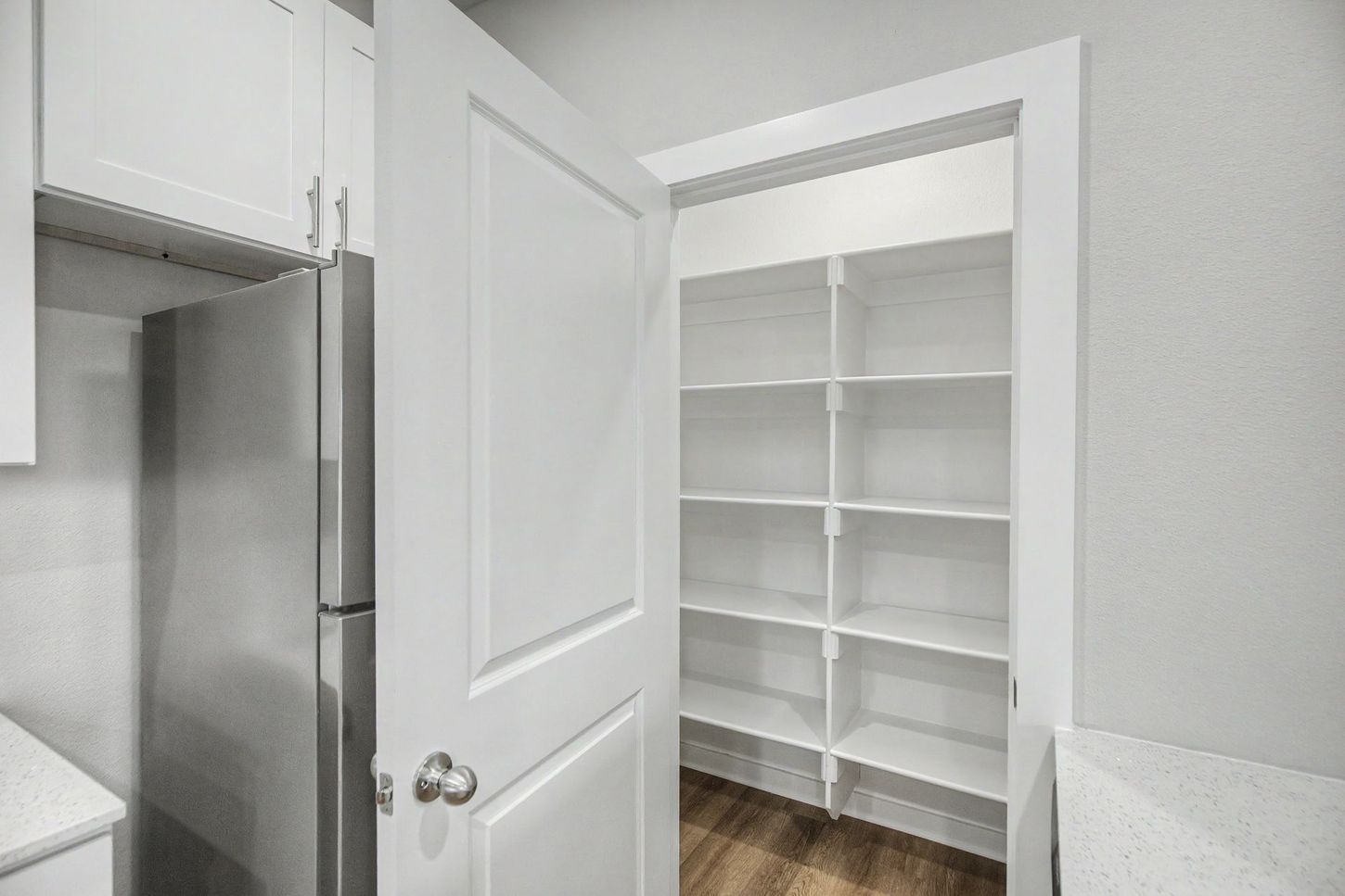 Open closet with white built-in shelves and cabinets, seen through a white door in a bright room.