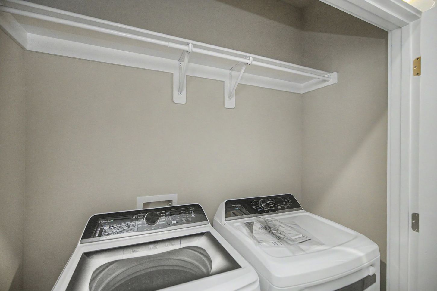 Laundry closet with a washer and dryer beneath a white shelf.
