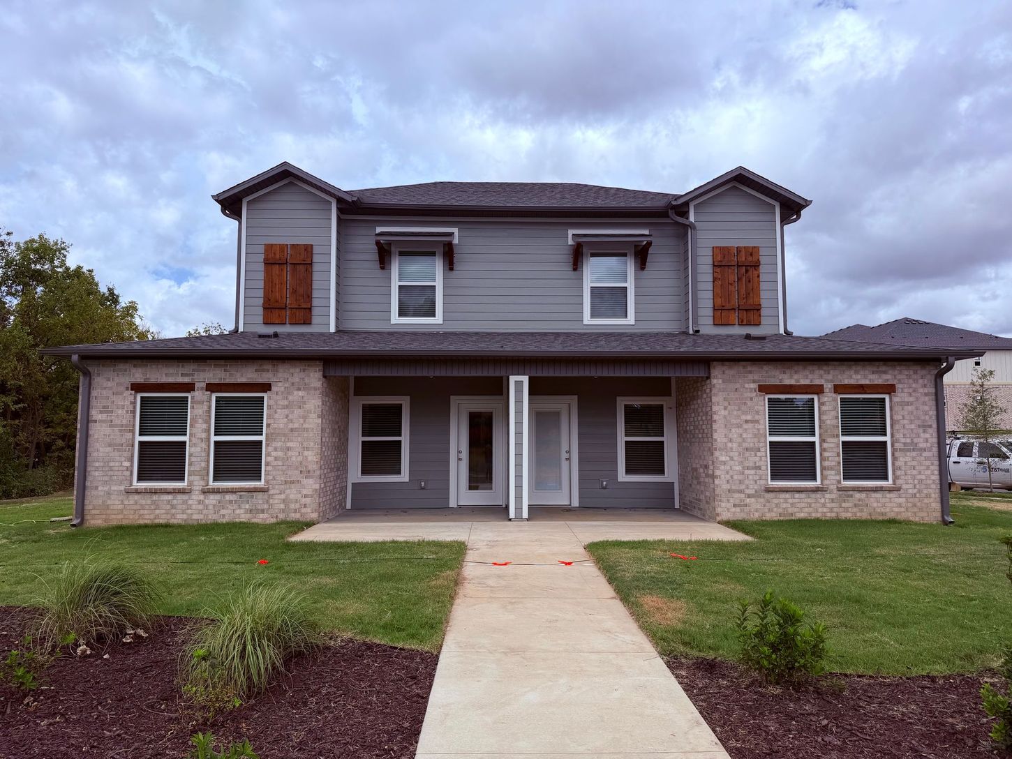 Two-story brick house with a central walkway and covered front porch under a cloudy sky