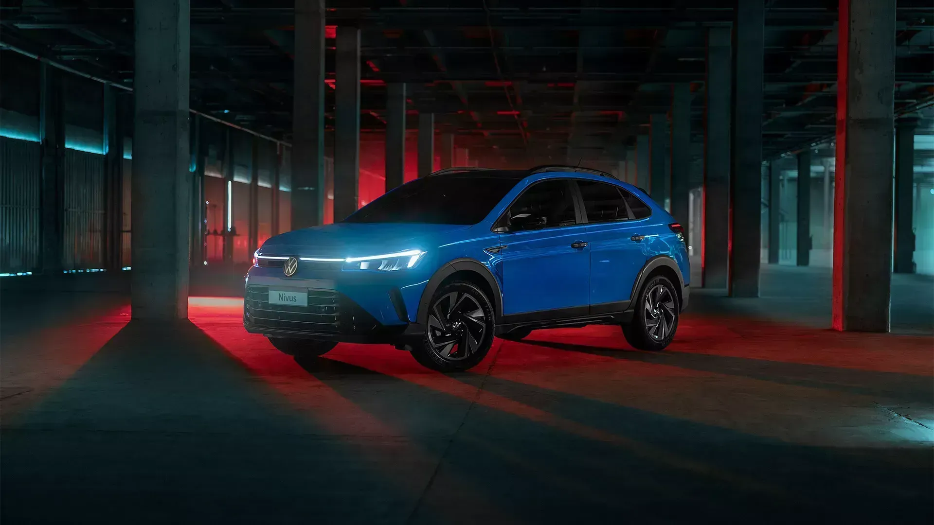 Um SUV azul brilhante estacionado em um espaço industrial escuro de concreto com iluminação ambiente 