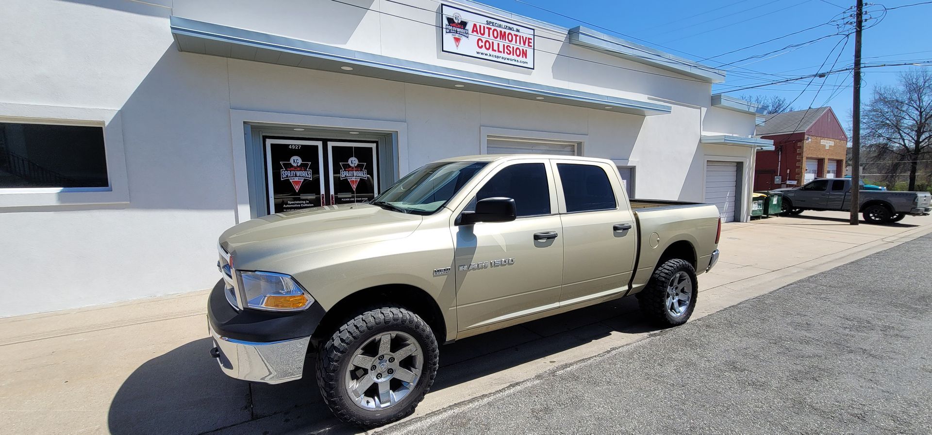 Tan pickup truck parked outside a white storefront on a sunny street.