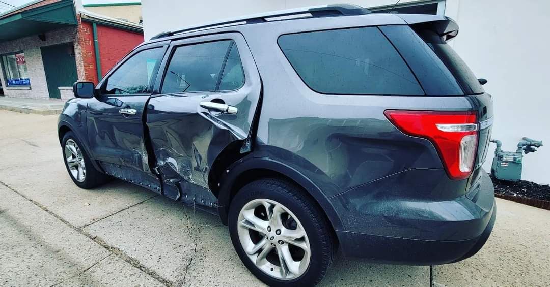 Dark SUV with heavy side damage parked beside a building on a sidewalk