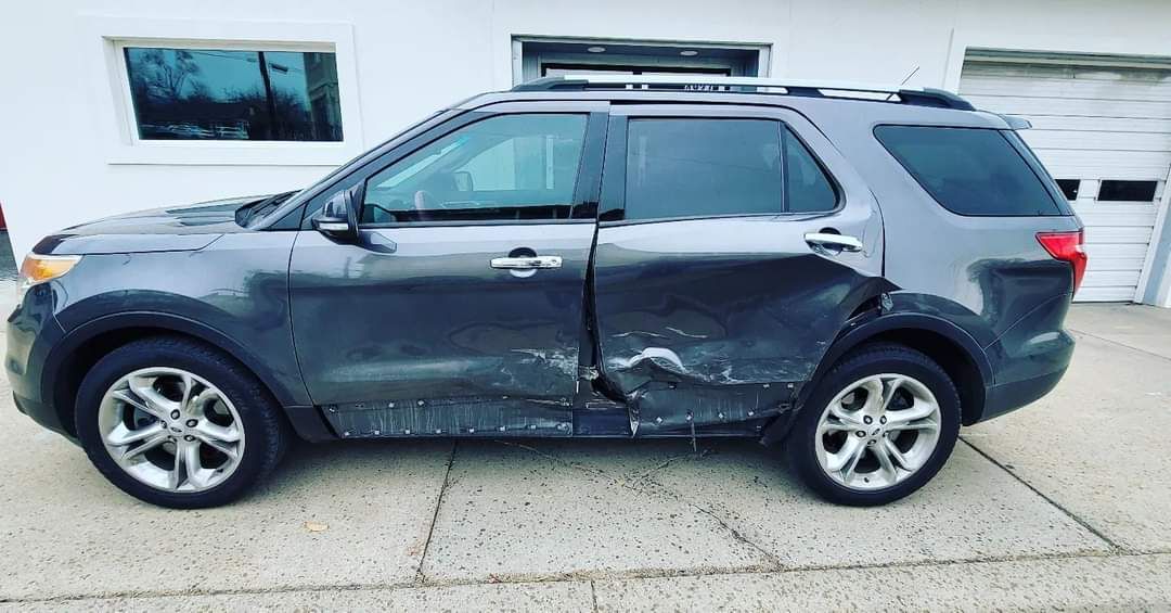 Damaged dark SUV with dented side, parked on a lot in front of a building.