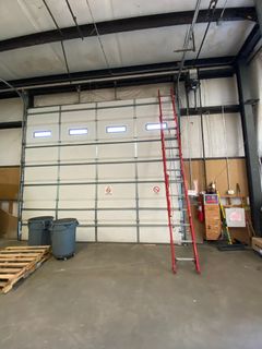 Red ladder leans against a closed, white overhead garage door inside a warehouse. 