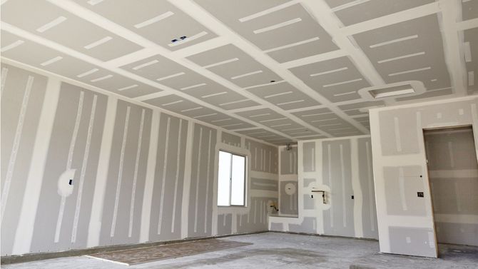 Empty drywall room under construction with taped seams, a window, and an open doorway