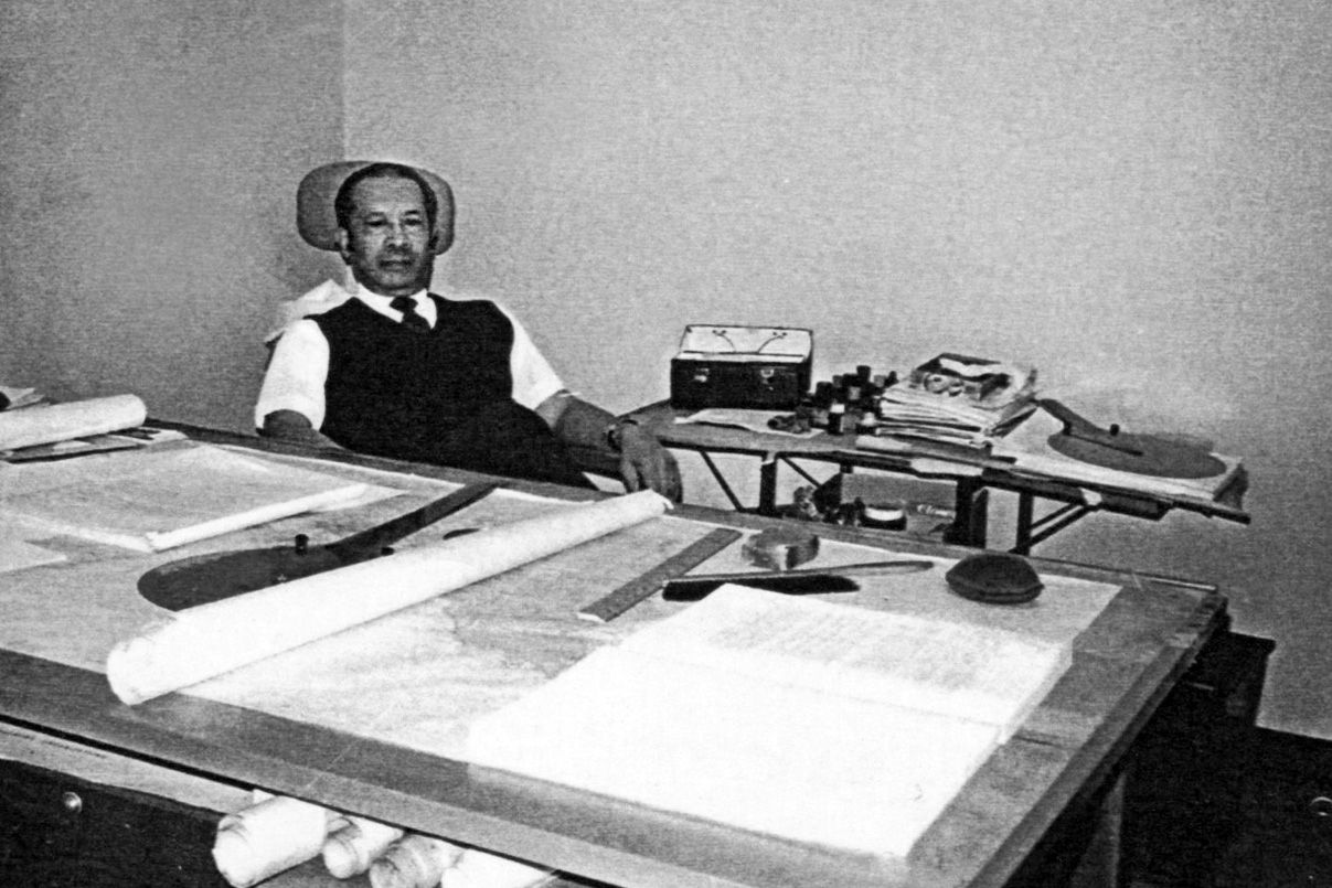 A man sitting at a desk with maps and cartography tools