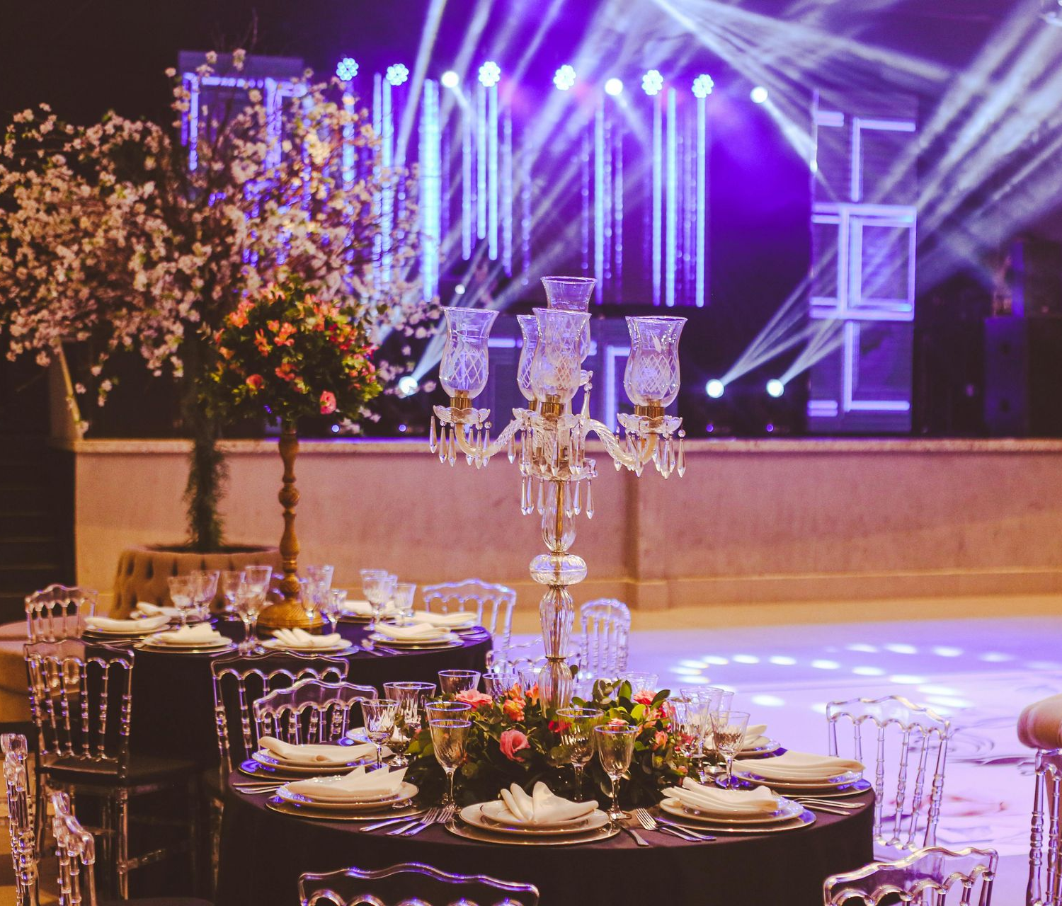 Elegant banquet table with floral centerpiece and candles in a purple-lit event hall