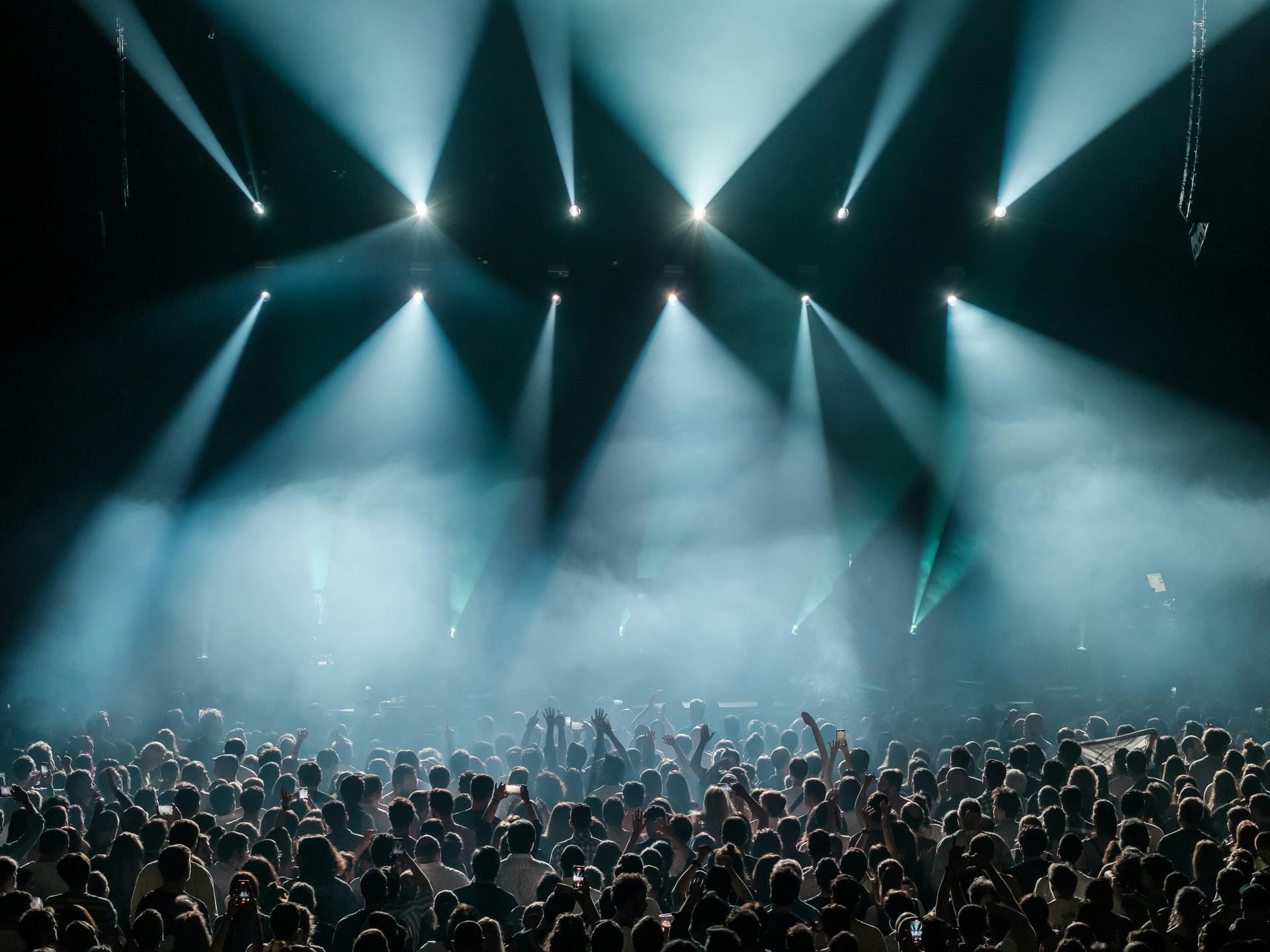 Crowded concert venue with bright blue stage lights and a cheering audience