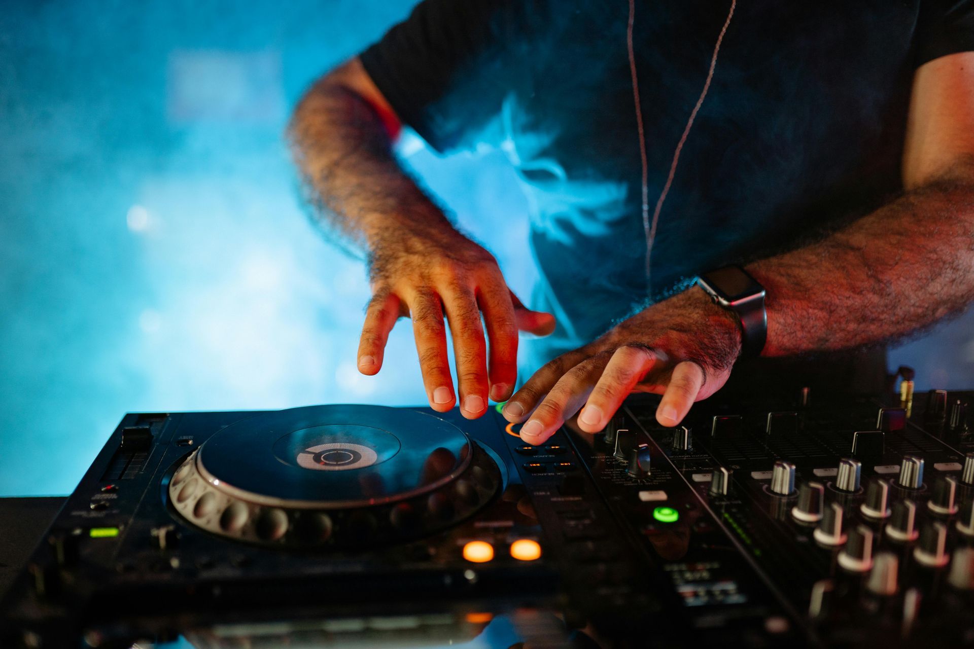 DJ mixing on a turntable and mixer, hands adjusting controls in blue stage lighting