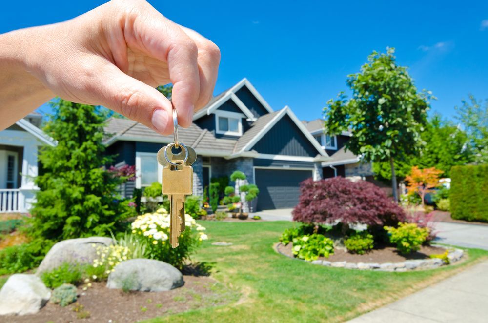 Hand Holding Keys in Front of a Blue House — Peterson Property Valuations Brisbane in Gold Coast, QLD