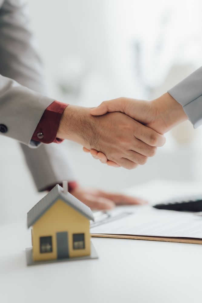 Two People Shaking Hands Over a House Model — Peterson Property Valuations Brisbane in Caloundra West, QLD