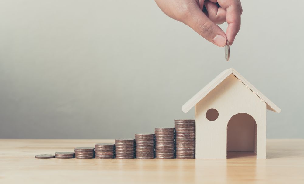 Hand Placing Coin on a Wooden House Model — Peterson Property Valuations Brisbane in Northern Growth Corridor, QLD