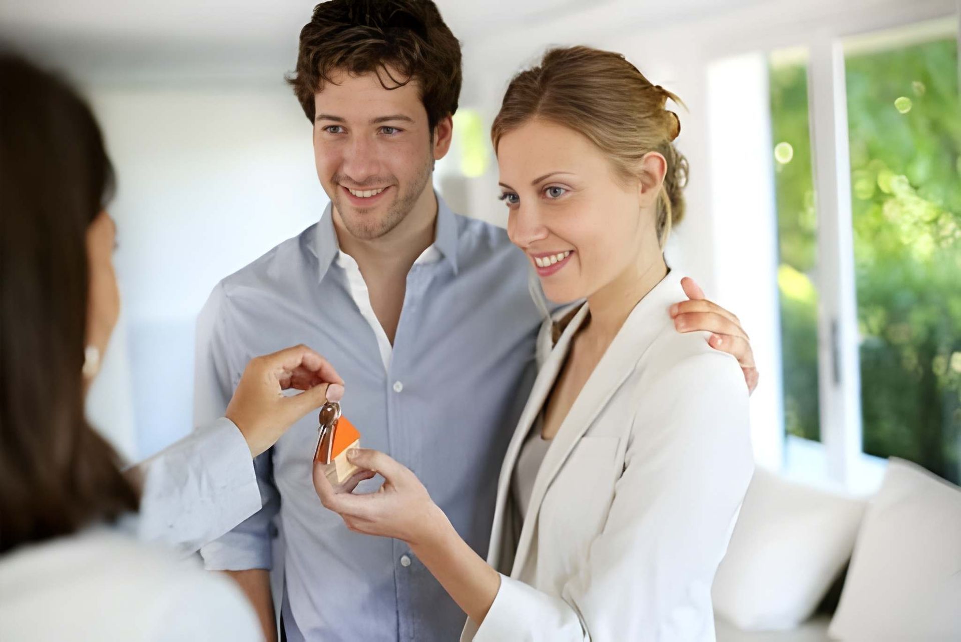Woman Handing Keys to Smiling Couple in Bright Living Room — Peterson Property Valuations Brisbane in Caloundra West, QLD