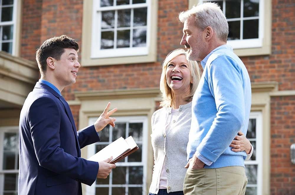 Real Estate Agent With a Couple in Front of a Brick House — Peterson Property Valuations Brisbane in Caloundra West, QLD